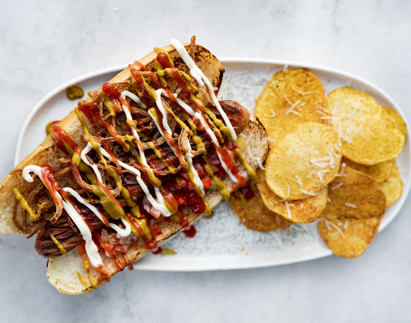 Hotdog bem recheado com salsicha, molho e acompanhamentos, servido com batatas