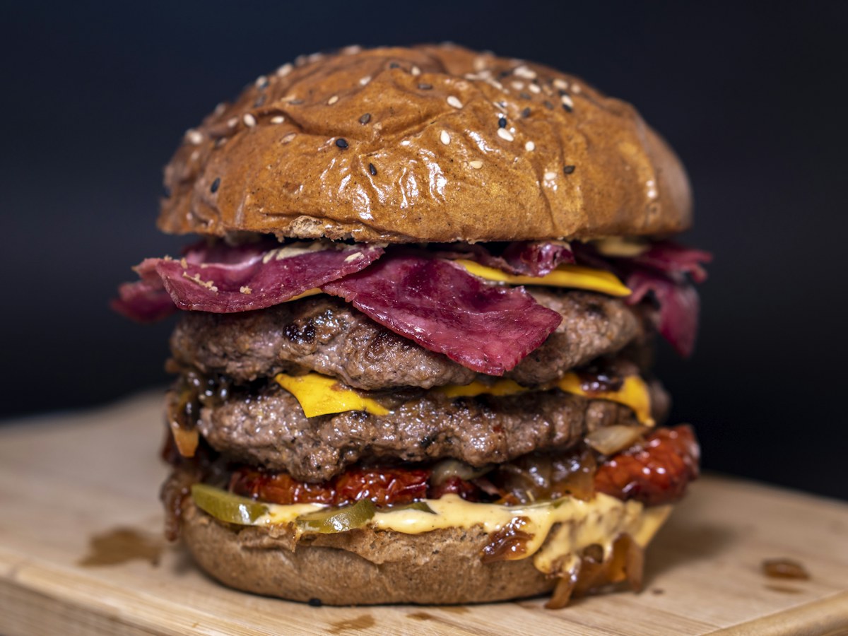 Hambúrguer artesanal alto, com camadas de carne, queijo e pão tostado